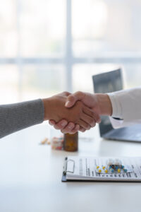 Medical service worker or doctor, pharmacist shaking hands with female medical patient at the table in clinic after giving advice on how to take medicine to the patient. health care service concept.